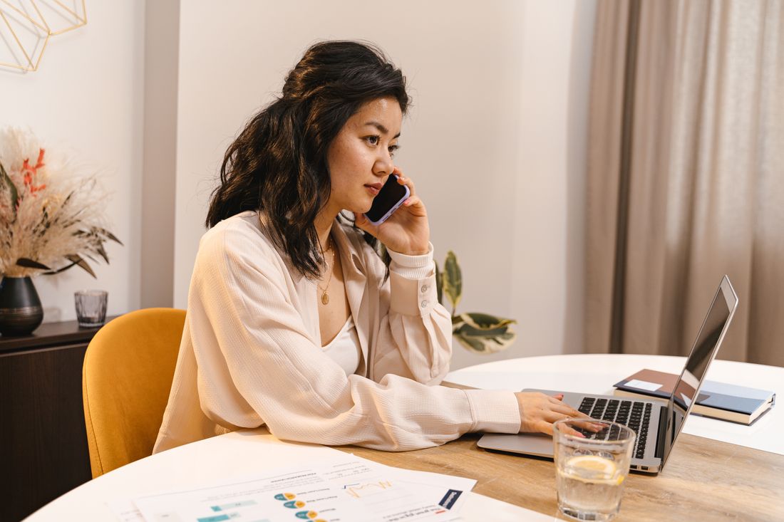 A woman working with a laptop and phone at a desk.